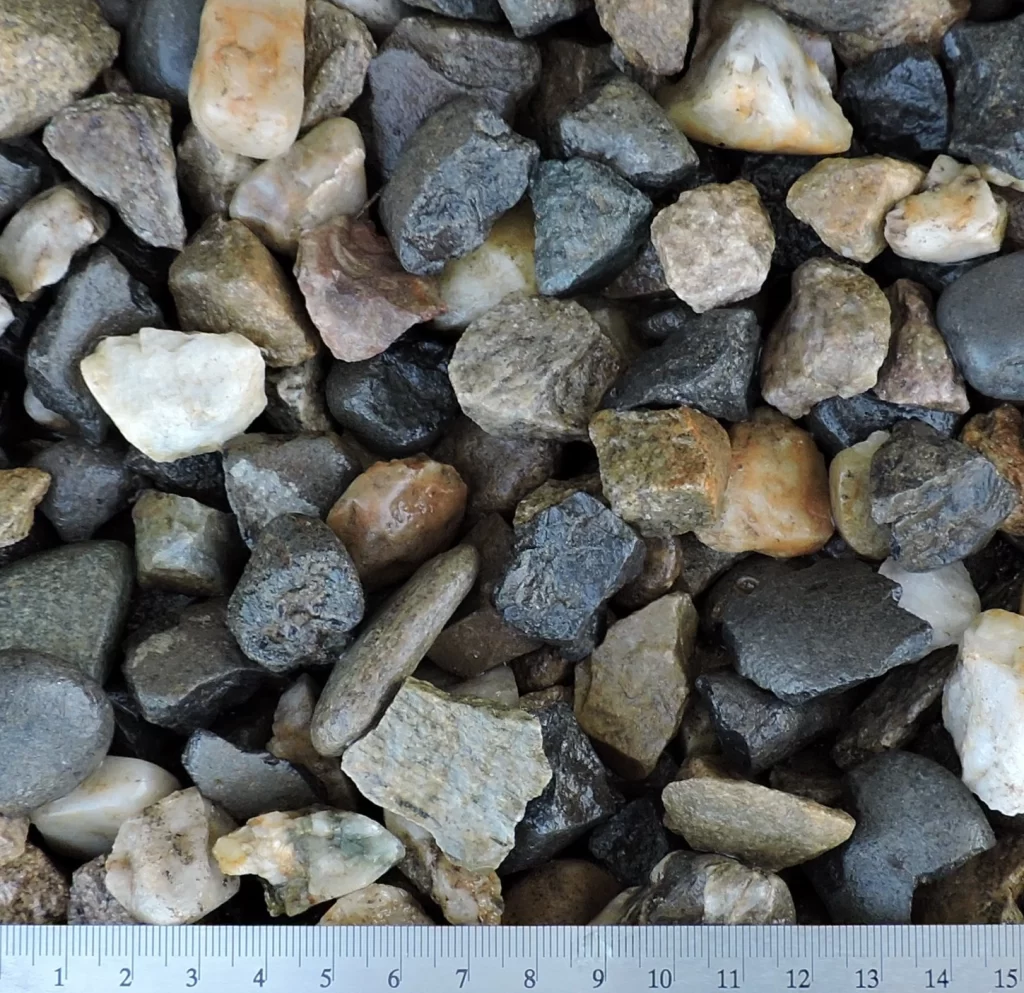 Detailní záběr na drcené kamenivo o velikosti 16–22 mm. Materiál obsahuje různě barevné kamínky různých tvarů a textur.